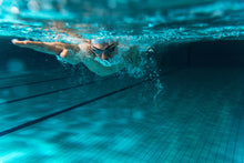 Load image into Gallery viewer, A male swimmer is captured underwater in a swimming pool, performing the front crawl stroke. This image could represent the experience of taking private adult swimming lessons in London. 
