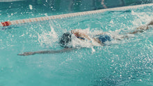 Load and play video in Gallery viewer, woman swimming freestyle in a clear blue pool, her body streamlined and powerful as she pulls her arm through the water. This image captures the focus and technique often taught in private adult swimming lessons, highlighting the importance of proper form and breath control.
