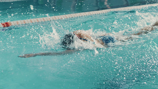 woman swimming freestyle in a clear blue pool, her body streamlined and powerful as she pulls her arm through the water. This image captures the focus and technique often taught in private adult swimming lessons, highlighting the importance of proper form and breath control.